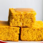 Stacked squares of gluten-free cornbread with a drizzle of honey on top on a red and white plate