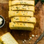 Overhead photo of gluten free potato bread sliced on wood board with herbs on top.