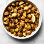 Air-fried baby potatoes in a white bowl garnished with parsley and a lemon slice.