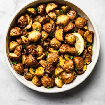 Air-fried baby potatoes in a white bowl garnished with parsley and a lemon slice.