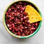 Green bowl filled with cranberry salsa with a tortilla chip tucked into the side.