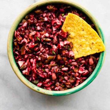 Green bowl filled with cranberry salsa with a tortilla chip tucked into the side.