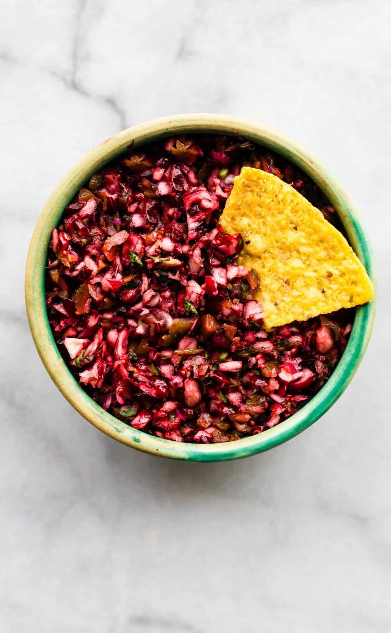 Green bowl filled with cranberry salsa with a tortilla chip tucked into the side.