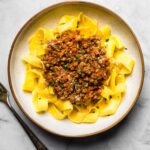 shallow bowl of gluten-free pappardelle with lentil bolognese on top and a fork on the side