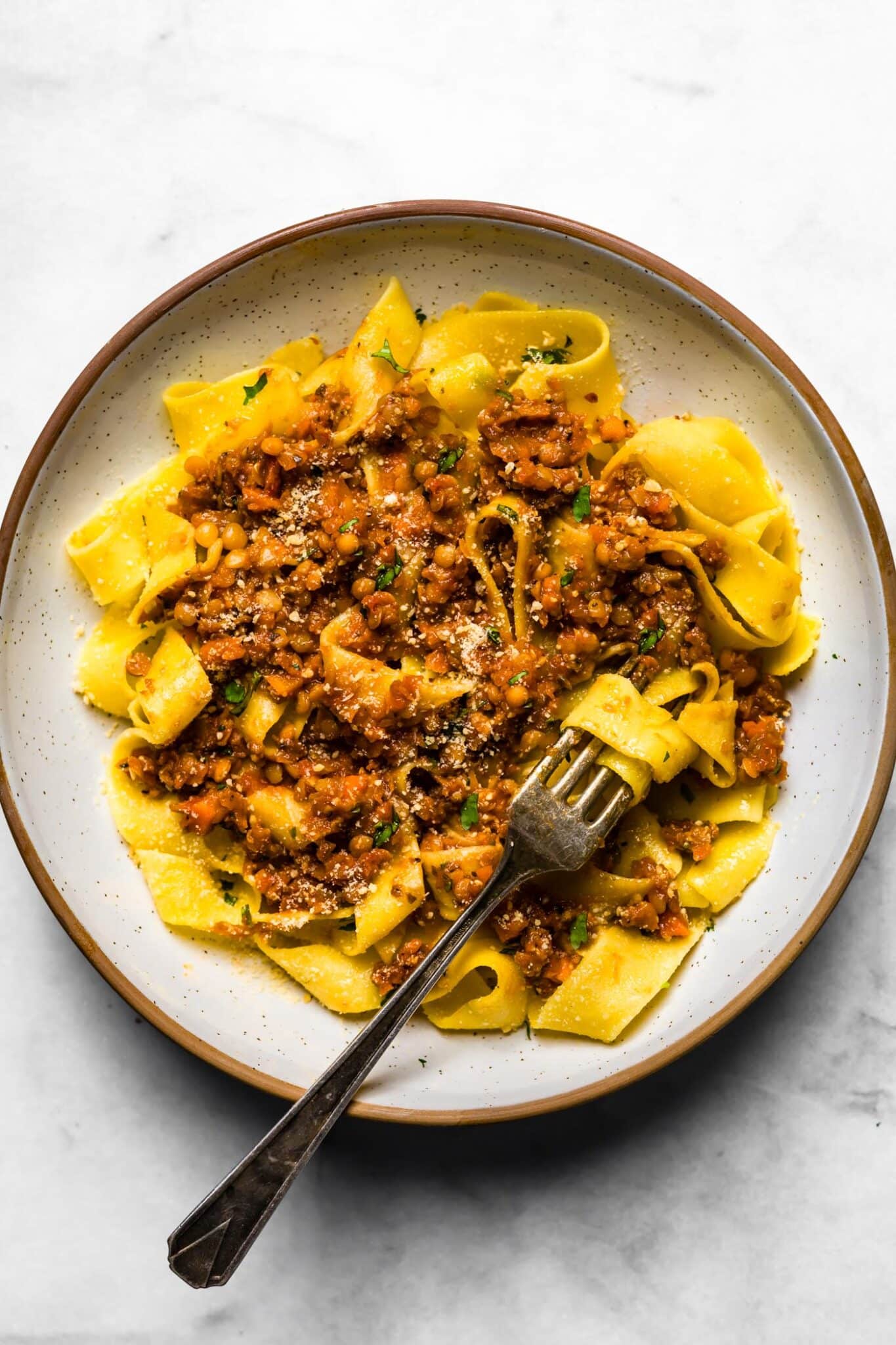 Shallow bowl of gluten-free pappardelle with lentil bolognese and a fork wrapped around pasta.