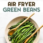 A photo of a serving bowl of air fryer green beans with 2 wooden serving spoons with text overlay for pinterest.
