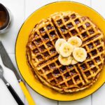 Gluten-Free Banana waffles with syrup and bananas, yellow plate, utensils