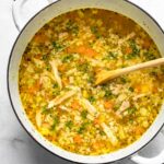 A pot of lemon chicken and rice soup after thickening, with carrots, celery, and herbs visible