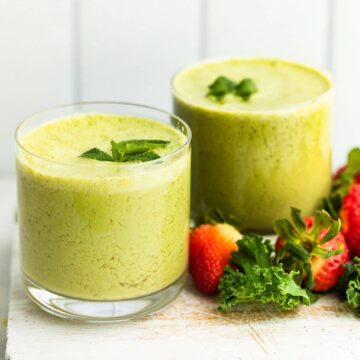 Two berry and kale smoothies prepared with fresh mint leaves, surrounded by strawberries