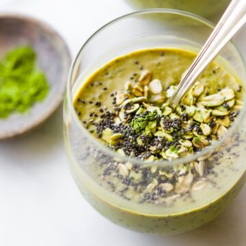 A chia matcha smoothie topped with chia seeds and oats in short drinking glass with a spoon.