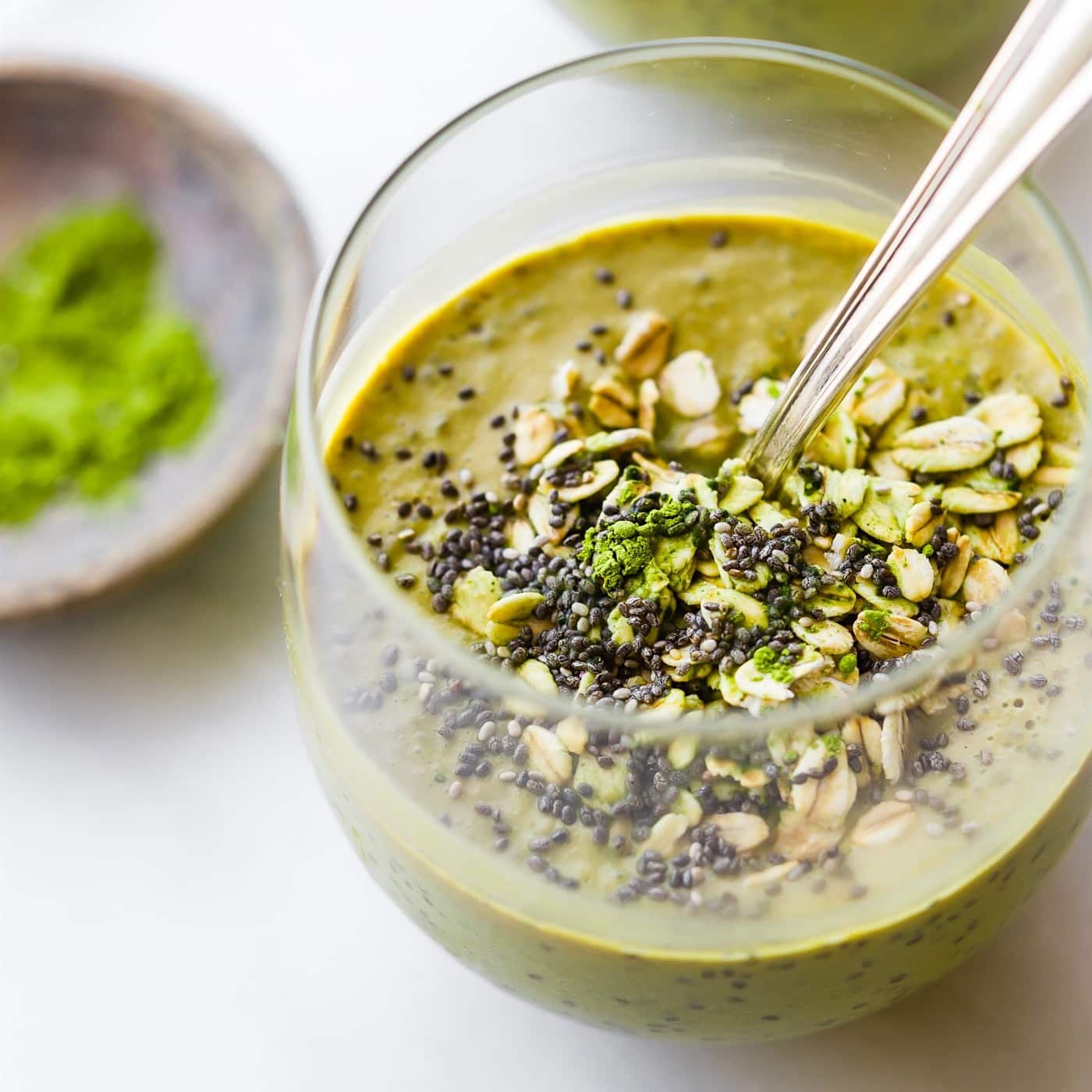 A chia matcha smoothie topped with chia seeds and oats in short drinking glass with a spoon.