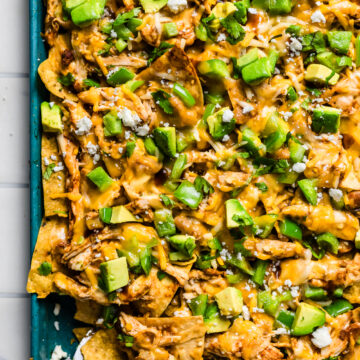 Close-up of cheesy sheet pan chicken nachos being lifted with a spatula, showing layers of chips and chicken.