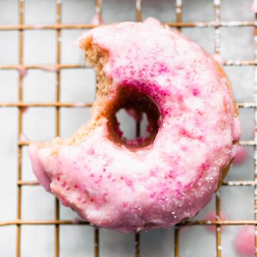 A gluten-free strawberry donut with pink icing with a bite missing