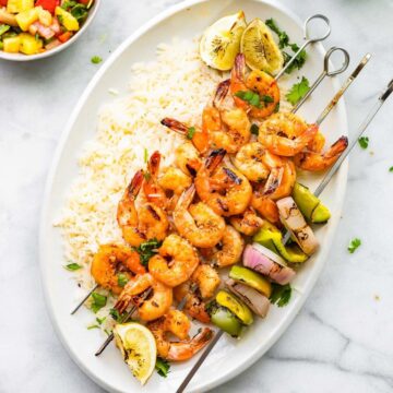 A photo of a white oval platter of Chile Ginger Shrimp Skewers over rice.
