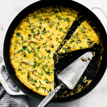 Baked vegetable frittata in a cast iron pan with serving utensil and a separated slice.