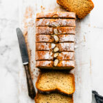 Sliced gluten-free Earl Grey cake loaf arranged on a board with powdered sugar, sliced almonds, and a knife on the side