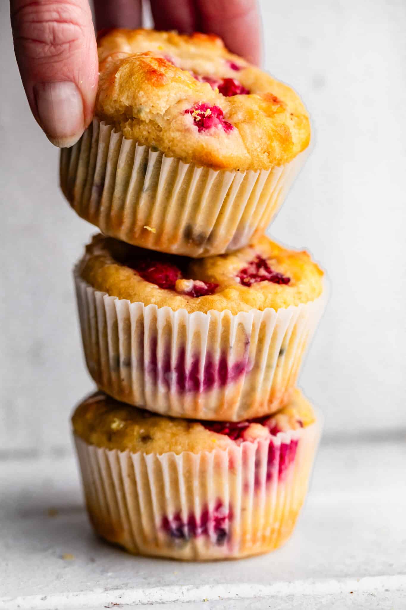Stack of 3 gluten-free lemon raspberry muffins and women's hand grabbing the top muffin