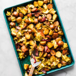 Large sheet pan of roasted cabbage, sausage, and crispy potatoes with spatula resting in it.