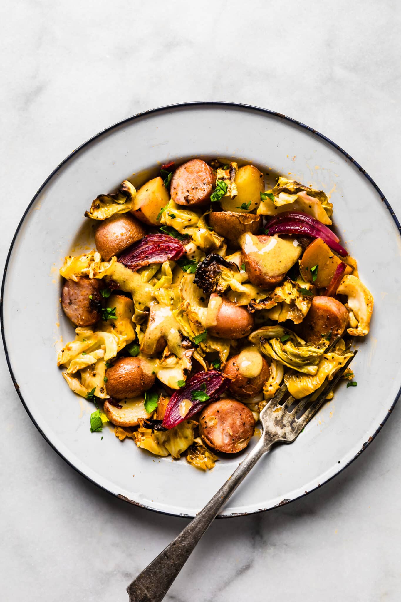 Cooked cabbage, sausage, and potatoes served in a bowl with a drizzle of dressing.