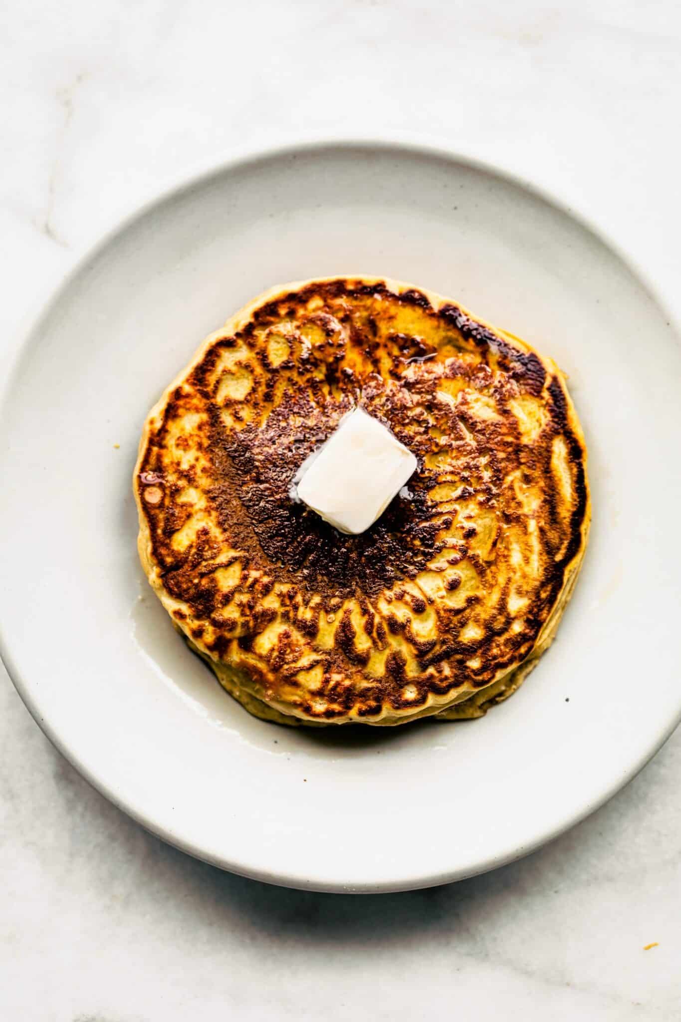 2. Stack of gluten-free pancakes on a white plate with a pat of butter melting on top.