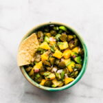 Small bowl of pickle and mango salsa topped with a tortilla chip on the side.