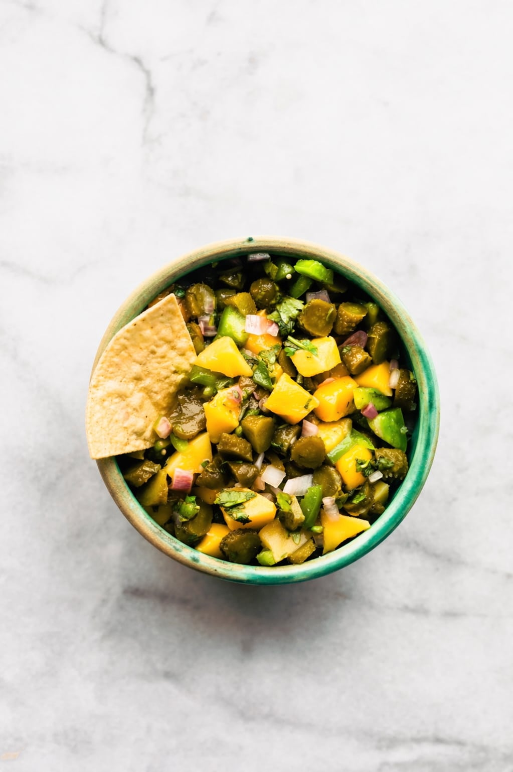 Small bowl of pickle and mango salsa topped with a tortilla chip on the side.