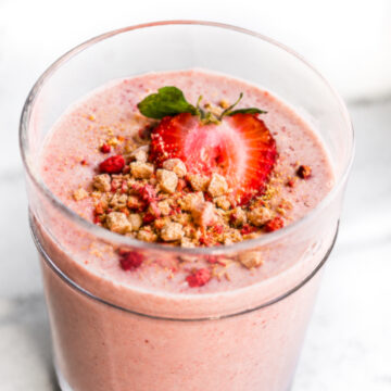 Finished strawberry smoothie served in a glass with strawberry and crumb topping.