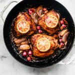 Roasted chicken thighs in a pan with caramelized shallots, chunks of rhubarb, and lemon slices on top.