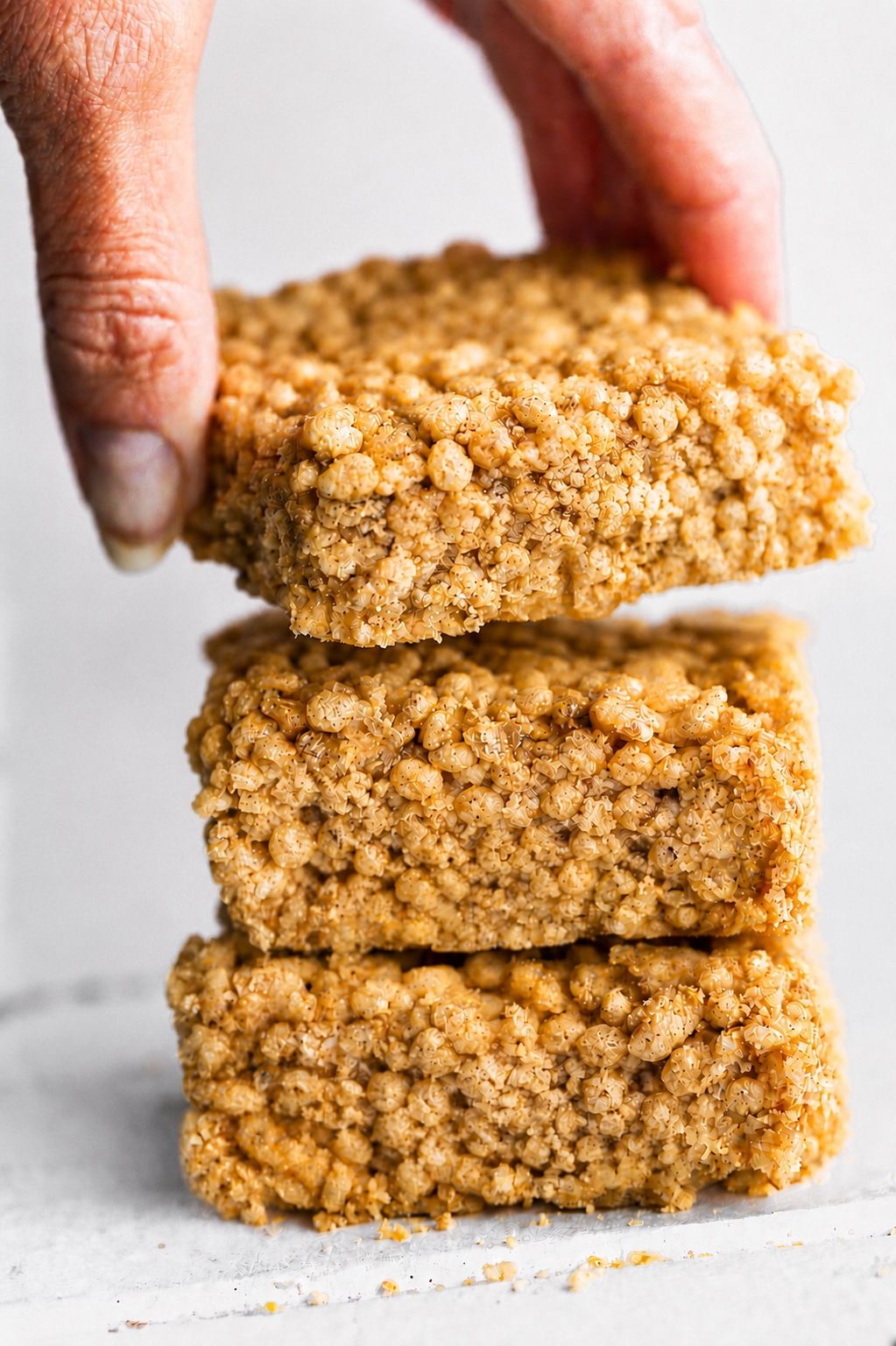 A hand holding a soft and chewy homemade rice crispy bar over a stack of sliced bars.