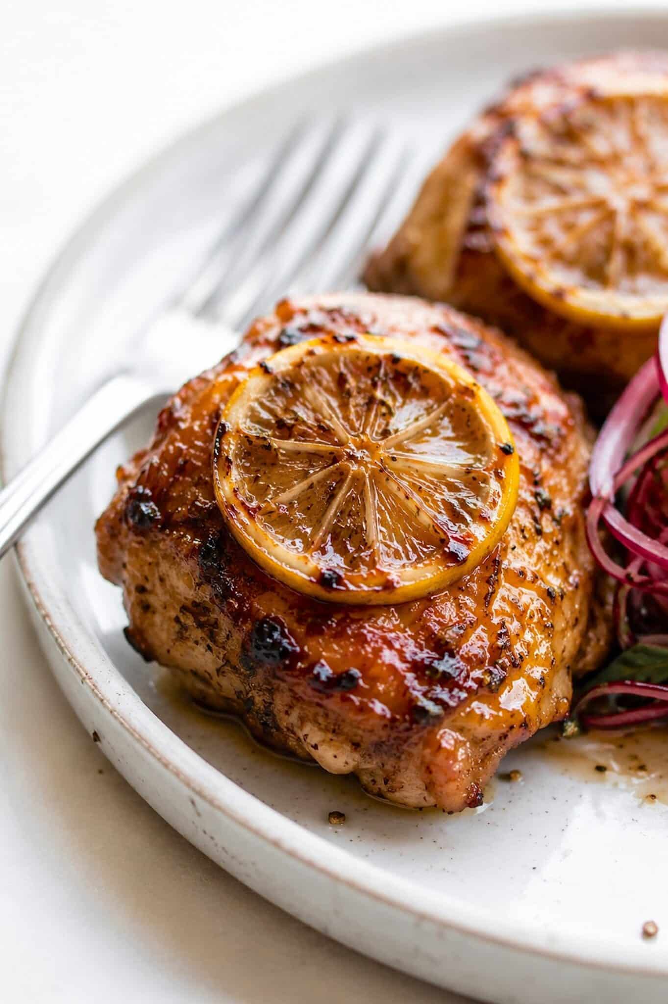 rhubarb marinated roasted chicken thigh with baked lemon on top and fork on the side