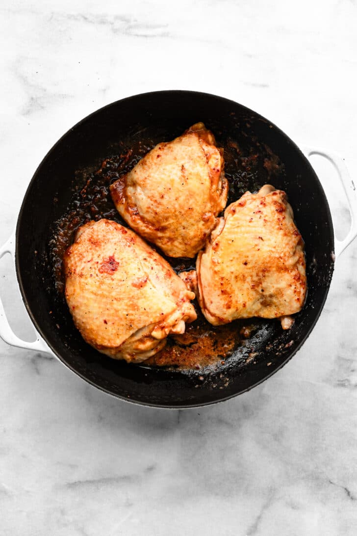 Chicken thighs coated in a red marinade in a skillet before cooking.