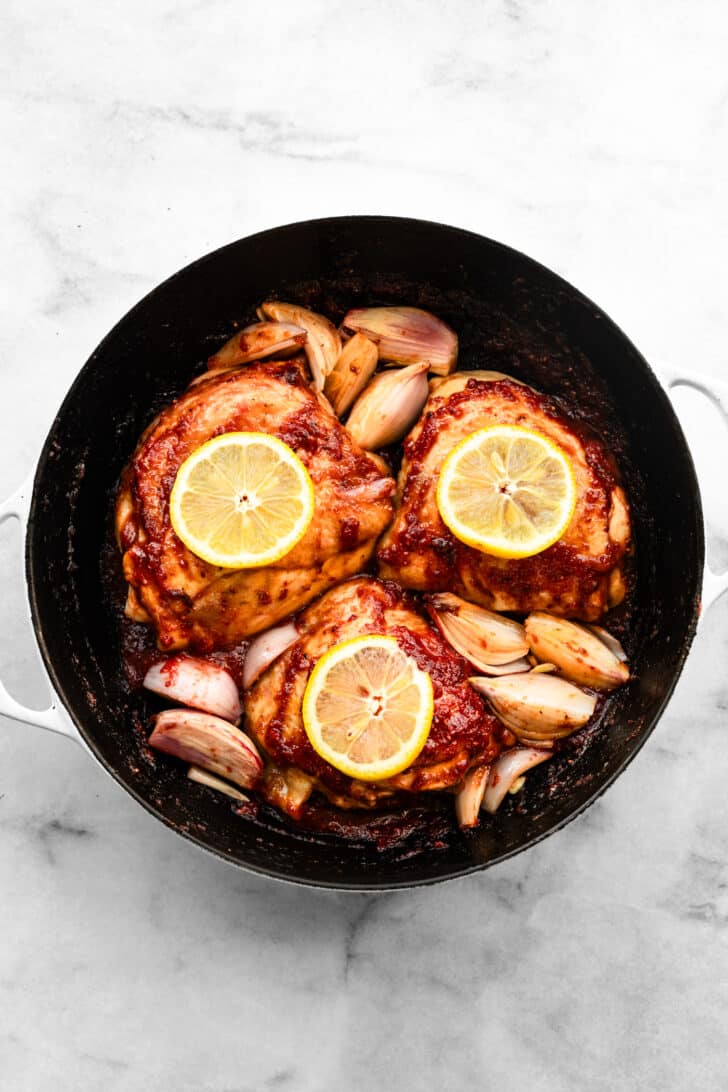 Chicken thighs roasted with lemon slices and softened shallots in a pan.