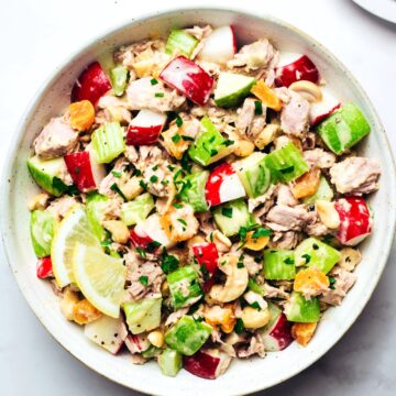 Finished tuna salad with chopped parsley, apples, celery, radishes, cashews, and tuna in a large serving bowl.