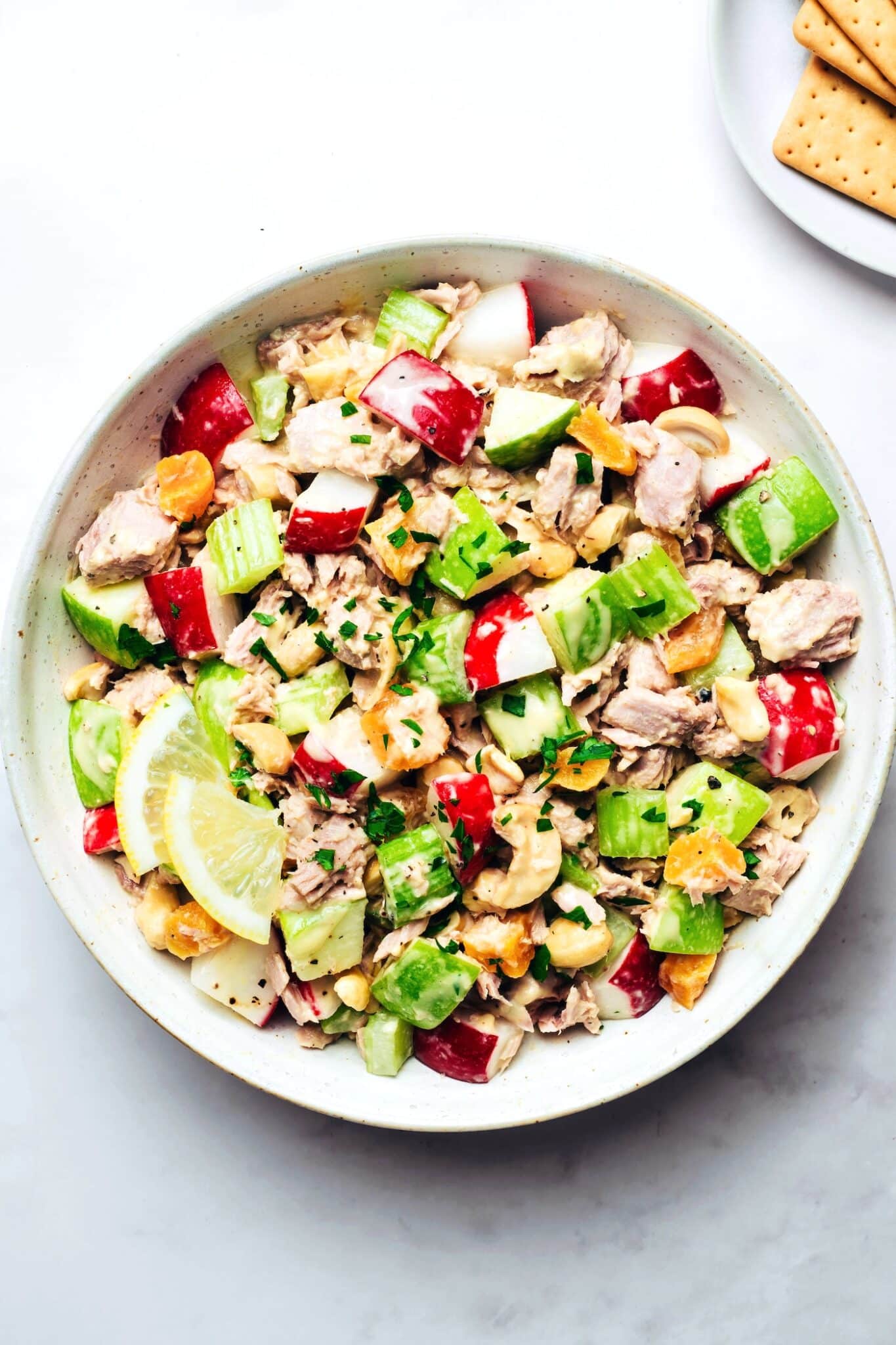 Creamy tuna salad with crunchy vegetables, cashews, and fresh herbs served in a bowl with lemon slices.