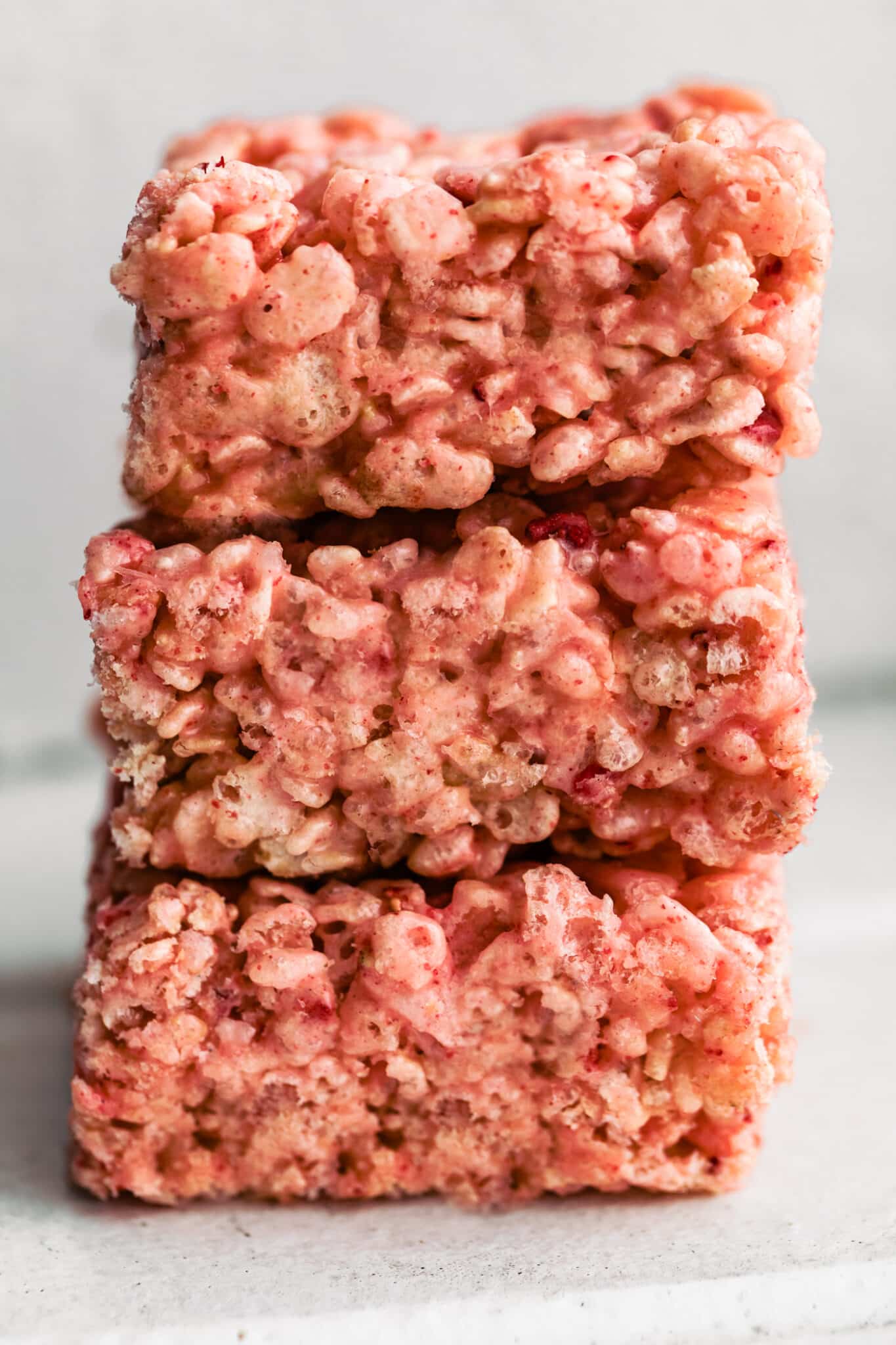 Close-up of stacked strawberry rice cereal treats with a pink marshmallow coating and freeze-dried strawberry pieces.