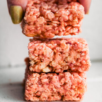 Hand lifting a strawberry rice cereal treat from a stack of three pink cereal bars.
