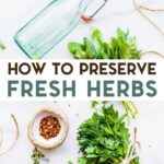 Ingredients and supplies for making infused herb vinegar (empty bottle, fresh herb bundles and red chili flakes) sitting on a white marble surface with a text overlay for Pinterest.
