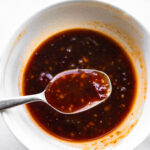 A spoon scooping up a spoonful of honey chipotle sauce out of a bowl