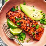 Plate of chipotle-glazed salmon surrounded by sliced avocado, lime, and fresh cilantro.
