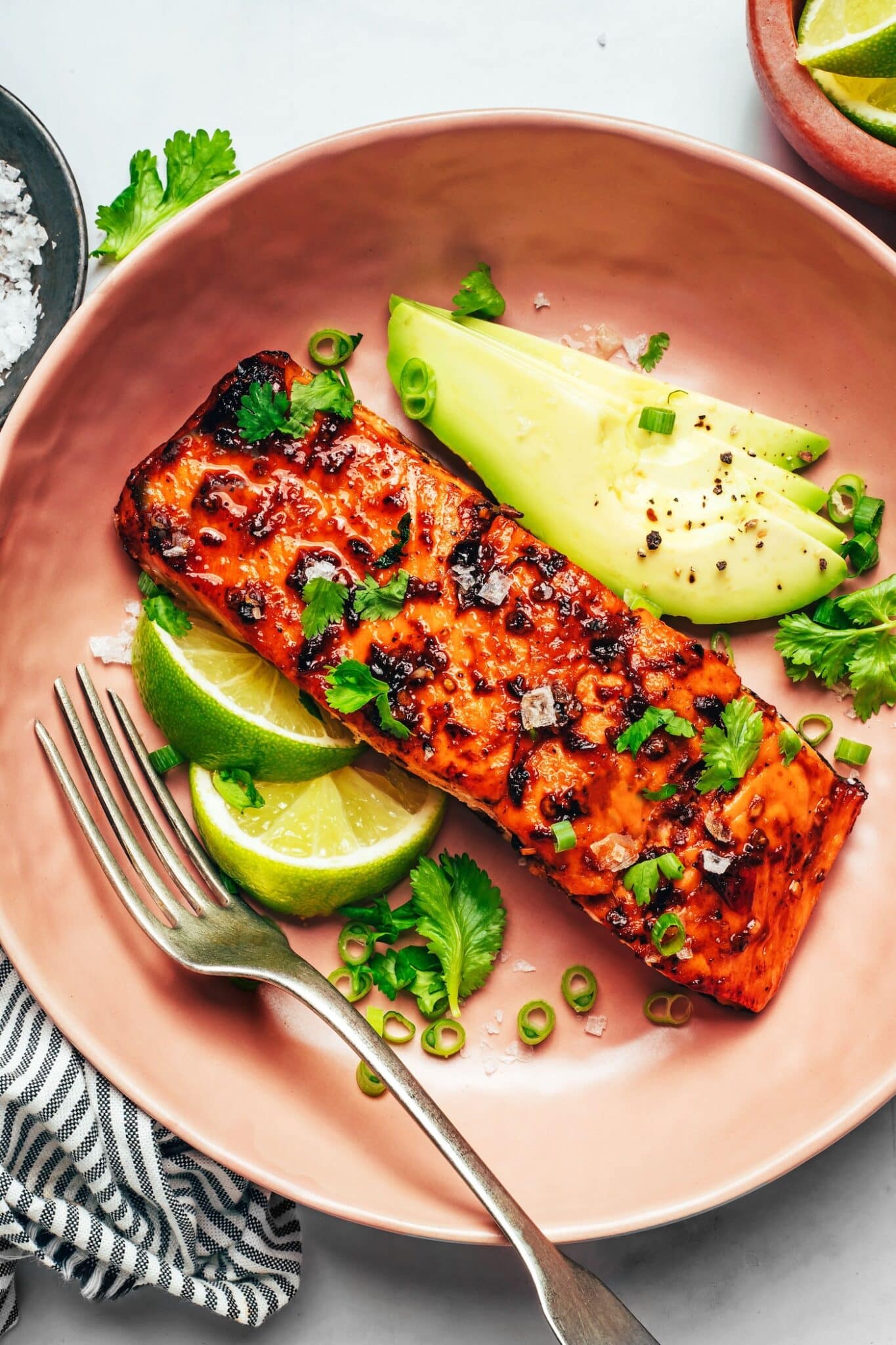 Plate of chipotle-glazed salmon surrounded by sliced avocado, lime, and fresh cilantro.