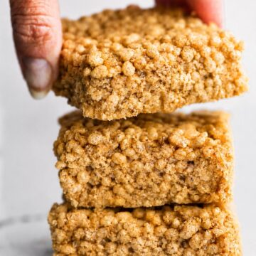 A hand holding a soft and chewy homemade rice crispy bar over a stack of sliced bars.