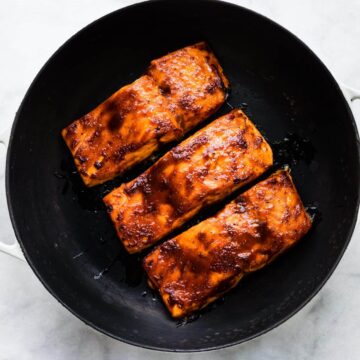 Overhead photo of three baked barbeque salmon filets in a cast iron skillet.