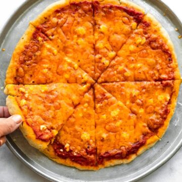 Overhead photo of a woman's hand picking up a slice of cheese pizza.